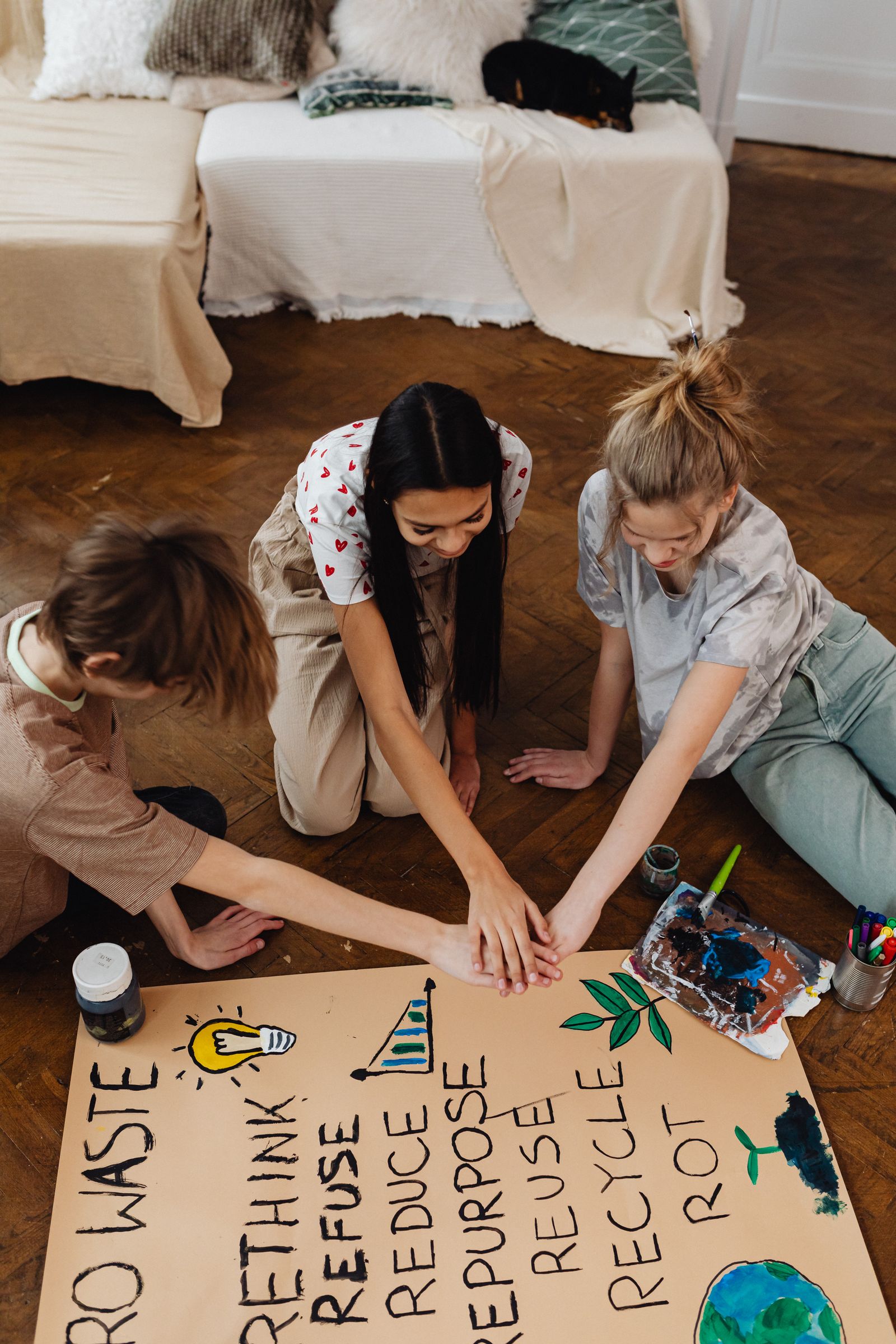 Three teenagers collaborate on a hand-painted recycling poster